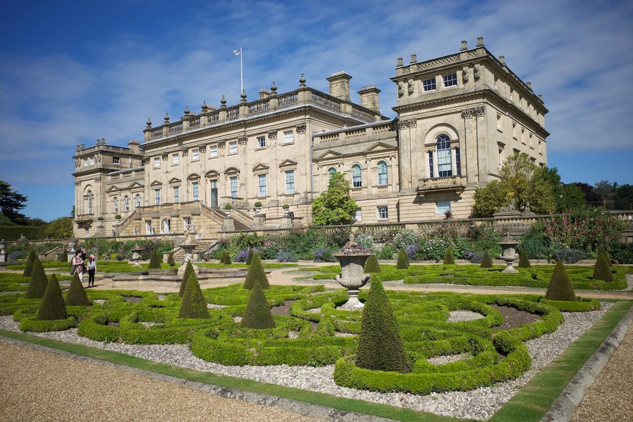 A beautiful view of Harewood House in England with ornate gardens under a clear blue sky.
