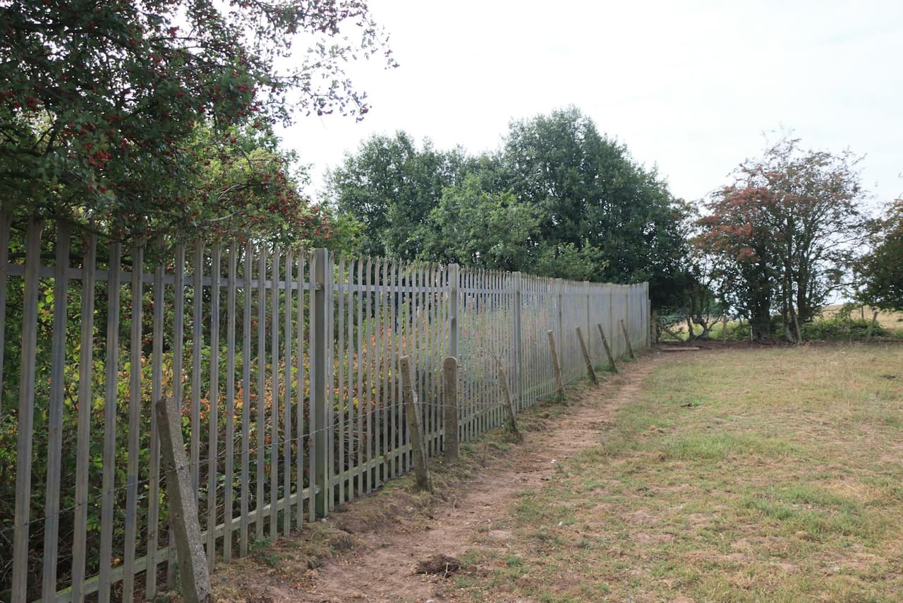 A rustic metal fence in a grassy field with trees in Audley, England.
