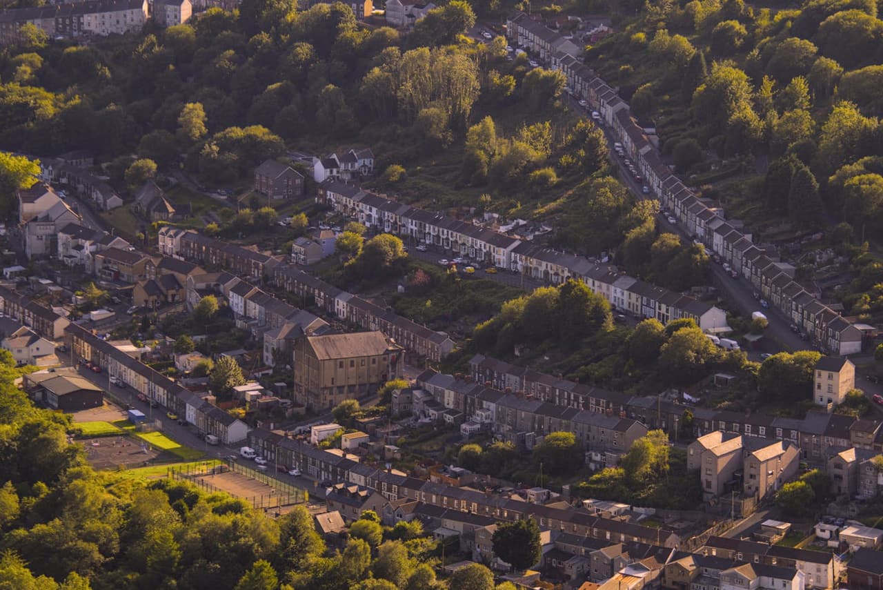 A picturesque aerial view of terraced houses amidst lush greenery in a Welsh valley.