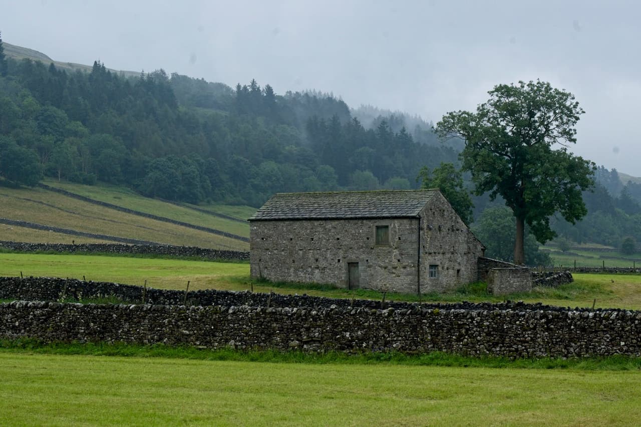 A serene stone farmhouse in Kettlewell, Yorkshire, surrounded by lush green fields and misty hills.